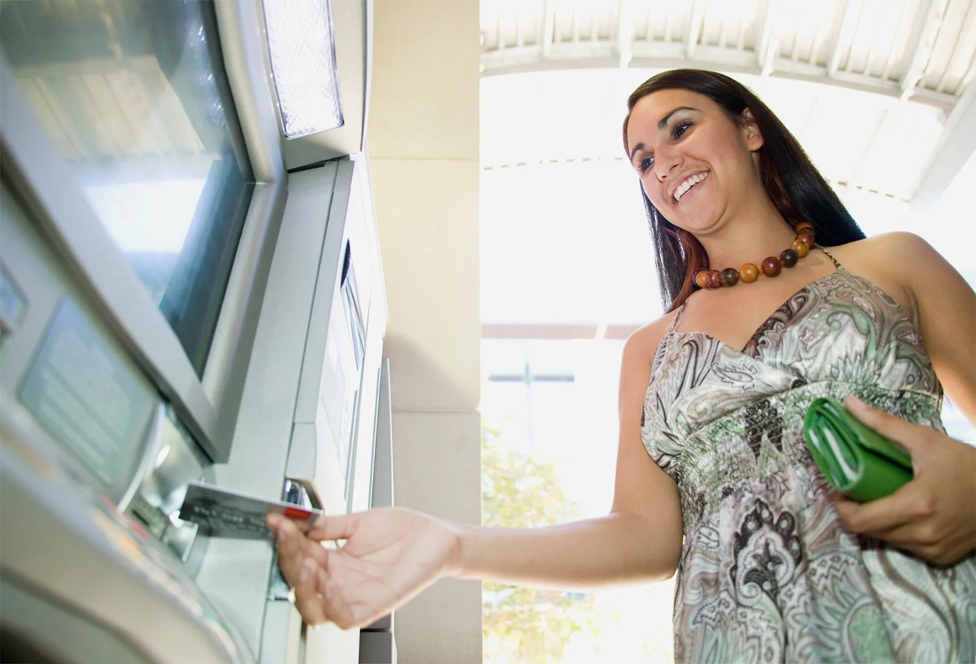 Woman using ATM, holding wallet, smiling.